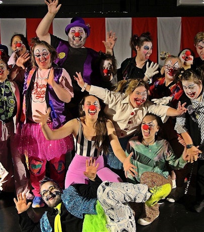 A group of artists dressed as clowns, smile with open arms showing enthusiastic body language.