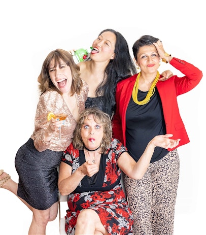 The Tight Mums are huddled together. Marilyn Leder is wearing a rose gold sequin top and black sparkly mini skirt, holding a cocktail and kicking up her heel, Pradeepa Timmermans is wearing a red floral dress and black choker and is lighting a joint, Lisa Lee is wearing a black sparkly dress and is chugging on a bottle of Tanqueray gin and Aarti Vincent is wearing tan leopard print pants, a red jacket and yellow beaded necklace and is running her hand through her hair while pouting.