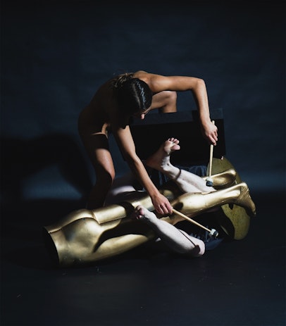 Two naked bodies pose in contortion amongst mannequin legs and drum mallets.