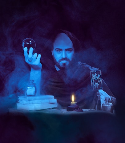 A performer wearing a cloak, seated a table and holding a crystal ball in one hand, and a tarot card in the other.