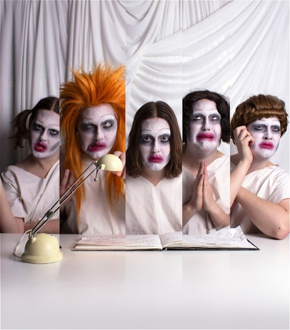 Performer sits in front of white curtain drapes at a desk, presented in 5 different variations of themselves, wearing different wigs and facial expressions in each variation, portraying 5 different personalities. 

Performer has white coloured foundation makeup, smudged lipstick and is wearing a white hospital gown.

On the desk is a hand written journal and lamp.