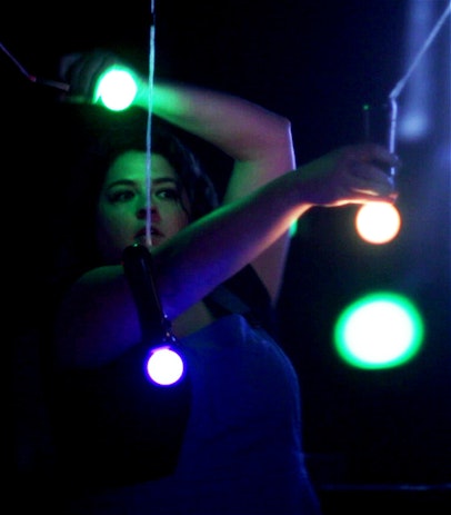 A woman holds two PlayStation move controllers with bright LED bulbs of different colors. Around her are more lit controllers, dangling by a string.