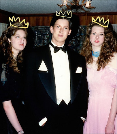 An AI generated image of three people in 80s formalwear (one in a black dress with long curly hair, one in a suit with two pocket squares, the third in a pink dress with blue neckscarf) in a lounge room. Their faces are distorted and blurred. They each have a yellow crown scribbled over their heads.