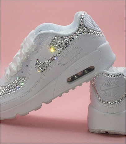 A pair of bejewled nike airs in front of a pale pink backdrop